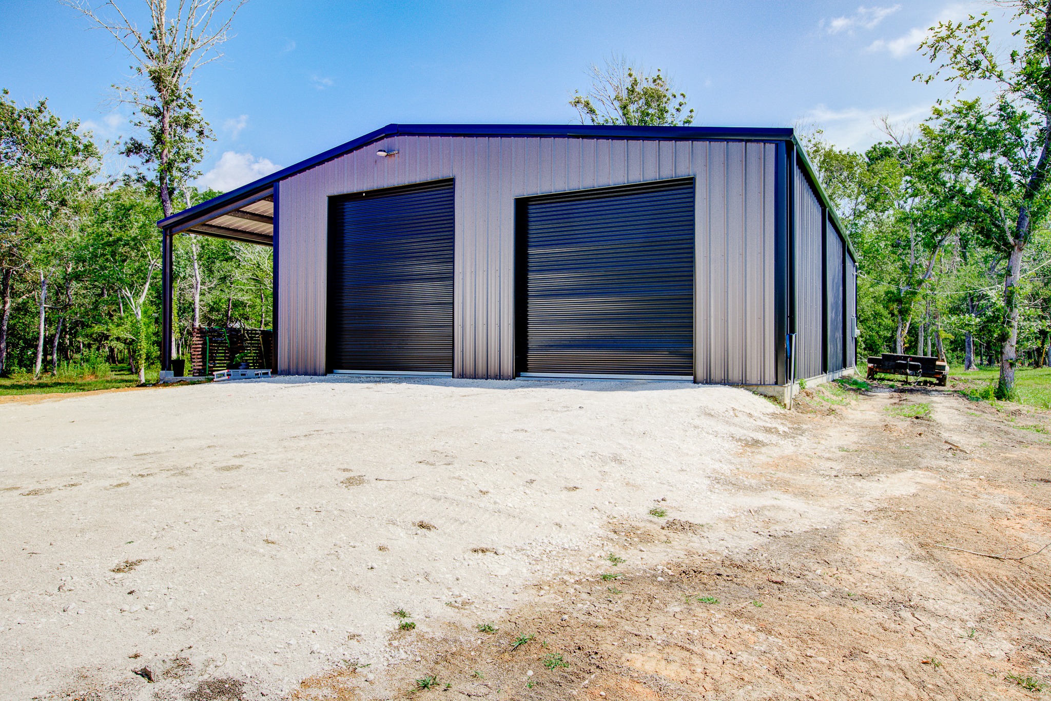Blue metal workshop building with two garage doors and gravel lot