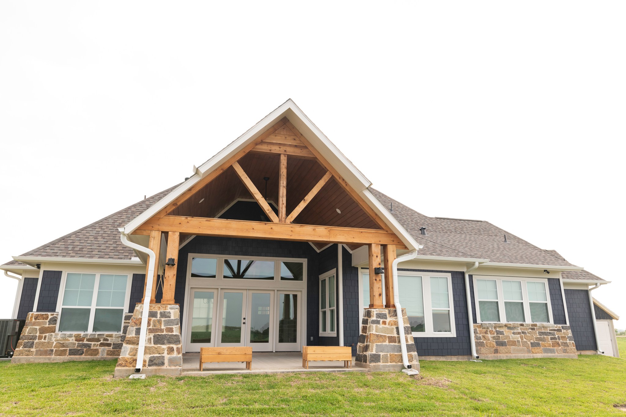 Front exterior of craftsman-style home with timber-framed entry, stone columns, and dark blue siding built by Hawkeye Construction in Sugar Land, TX