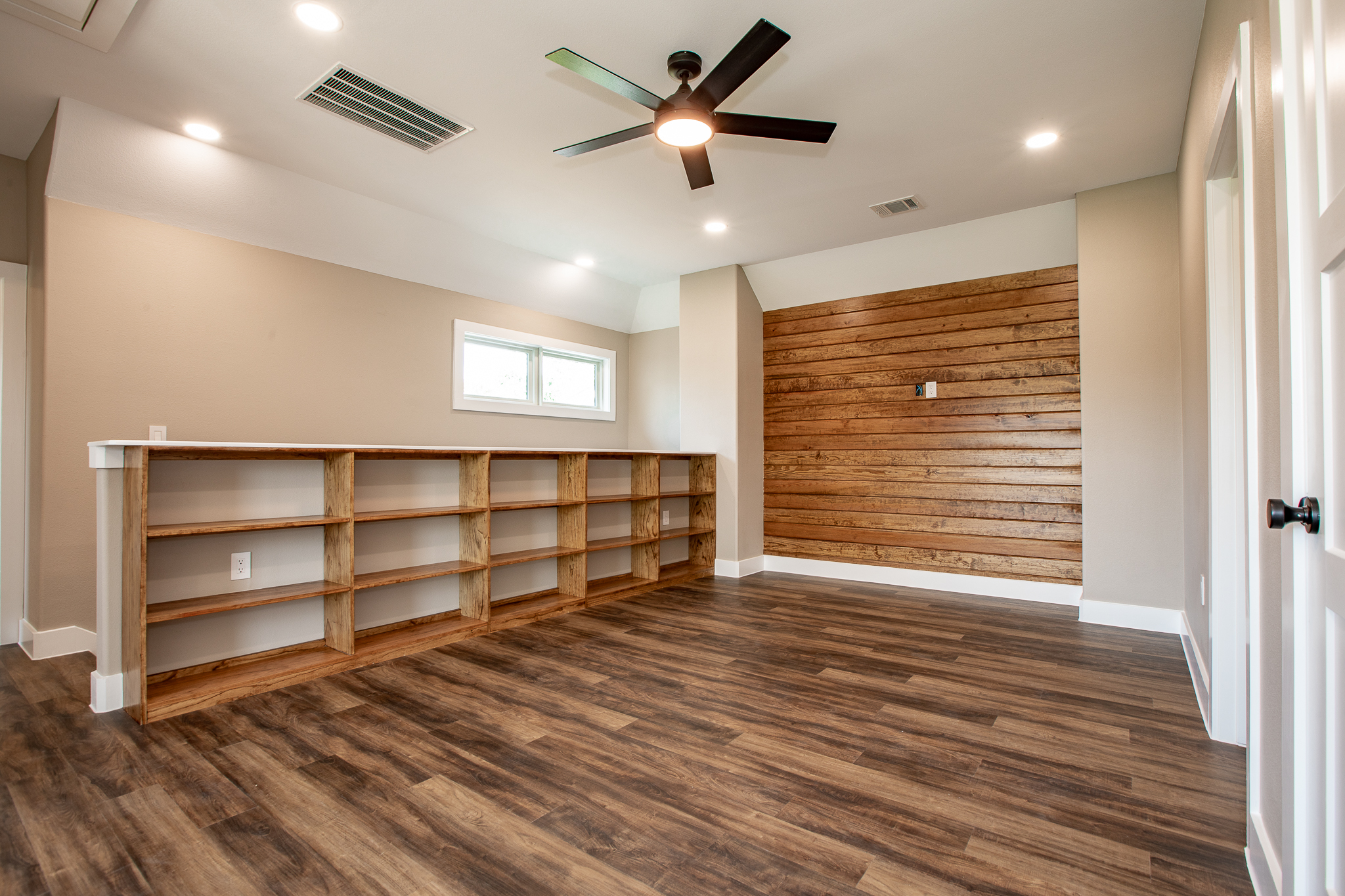 Large room with wood accent wall, ceiling fan, and built-in shelving
