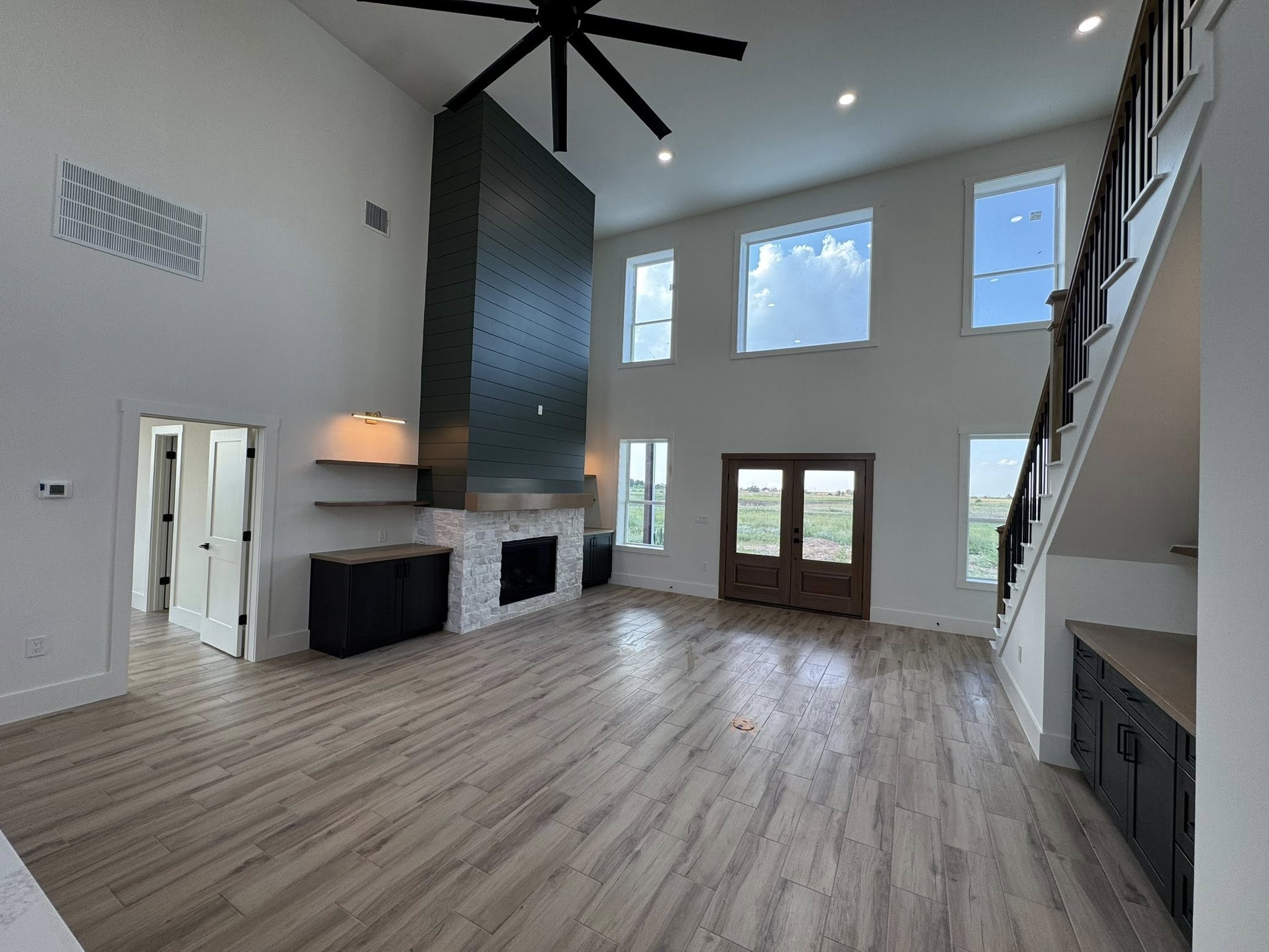 Modern living room with dark accent wall, ceiling fan, and tall windows