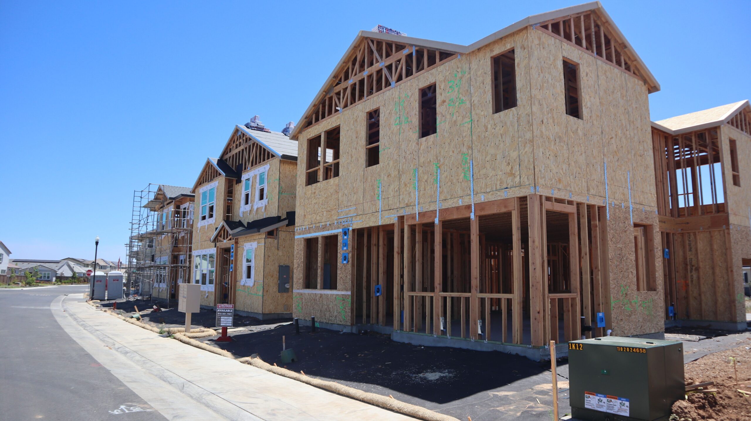 Wooden frames of modern houses in construction in Elk Grove, California, under clear blue sky.