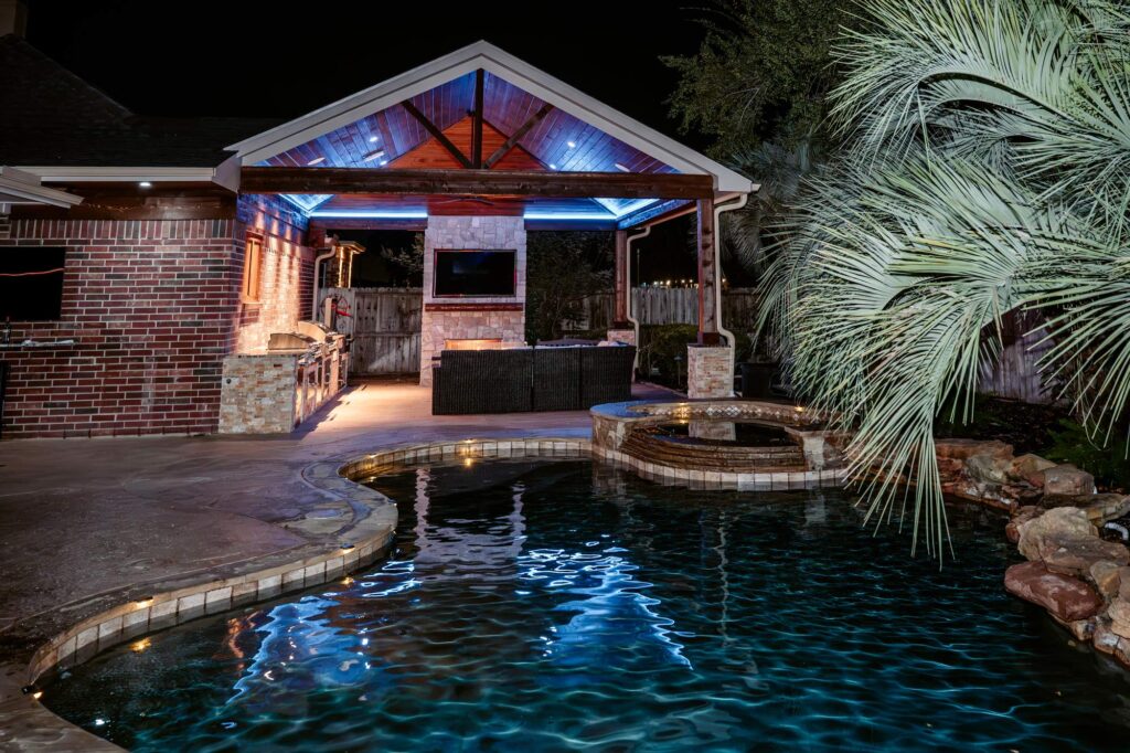 Covered outdoor kitchen pavilion beside a pool at night in Sienna, Missouri City