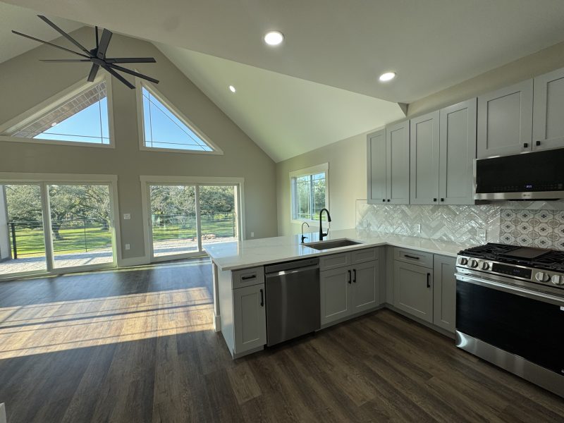 Modern kitchen with vaulted ceiling, large windows, and dark island