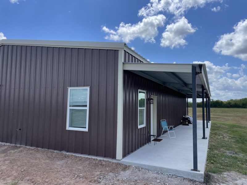 Dark metal barndominium with wraparound covered porch.