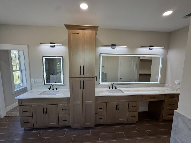 Double wood vanity with center linen tower and lit mirrors.