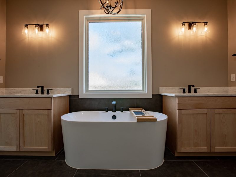 Freestanding tub between two wood vanities under window.