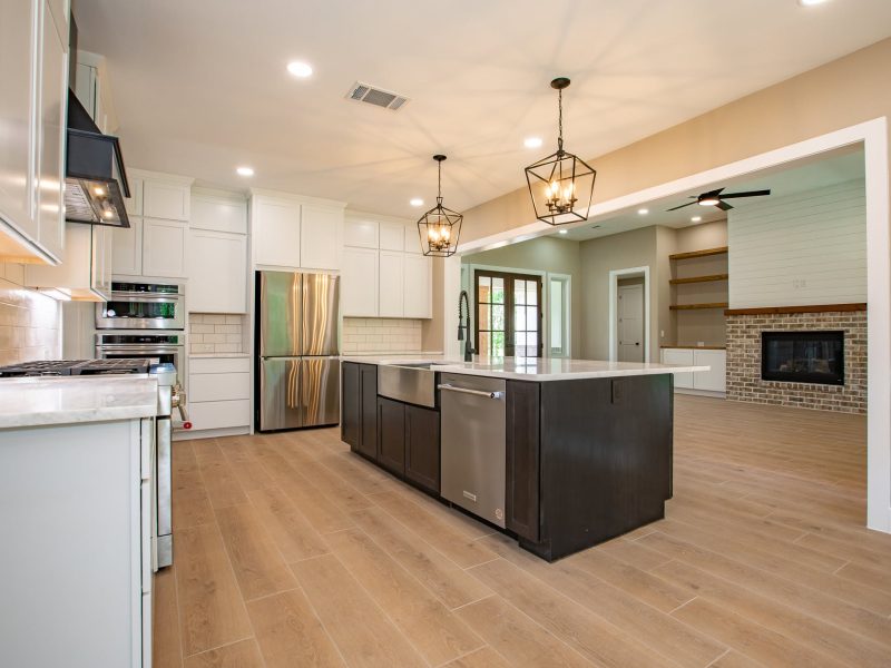 Open kitchen with dark island flowing into living room with brick fireplace.