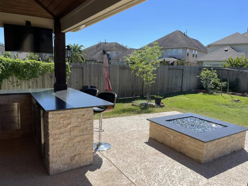 Outdoor bar with mounted TV beside fire pit.
