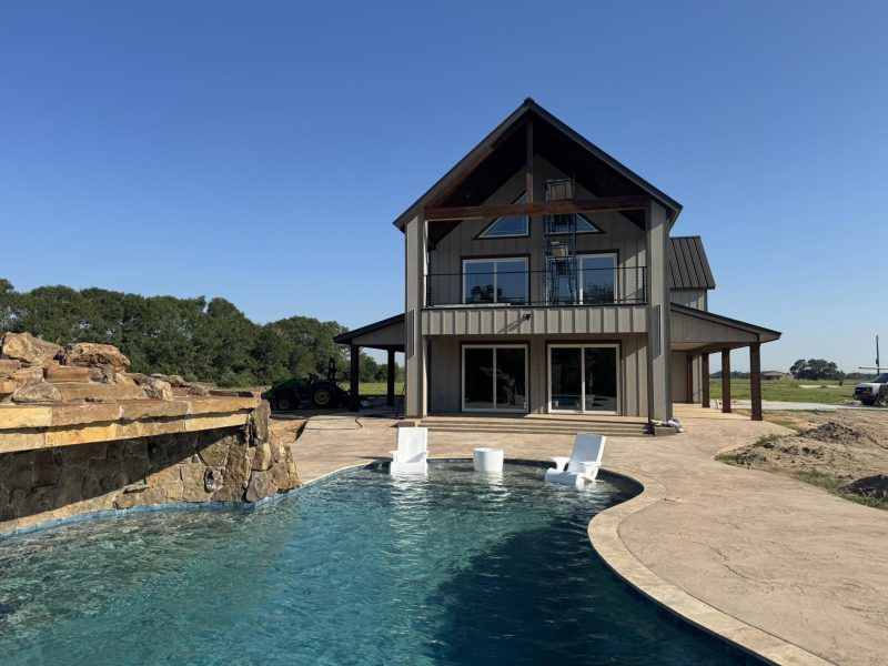 Pool with rock waterfall in front of two-story home.