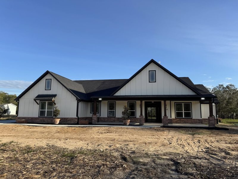 White farmhouse with black trim and a full-width front porch at dusk.