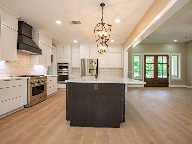 White kitchen with dark island, pro range and wood french doors.