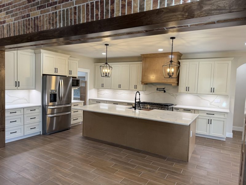 White kitchen with island seen through exposed brick archway.
