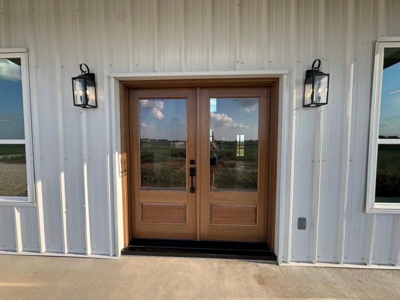 Wood double front doors with lantern sconces on white metal siding.