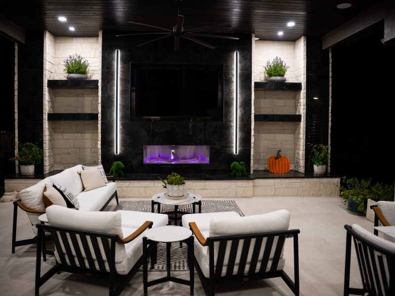 Modern outdoor patio with a sleek black fireplace, white cushioned seating, and stone accent walls.