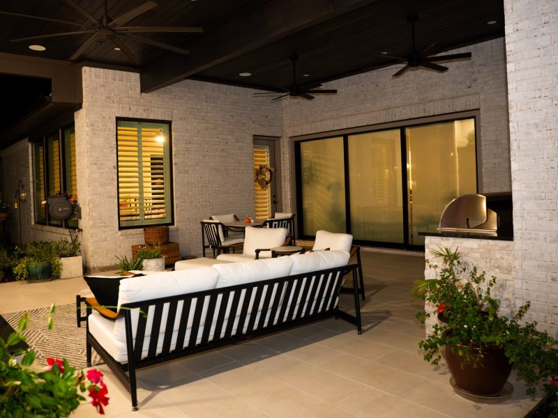 Covered patio with white brick walls, modern lounge seating, and a built-in grill.