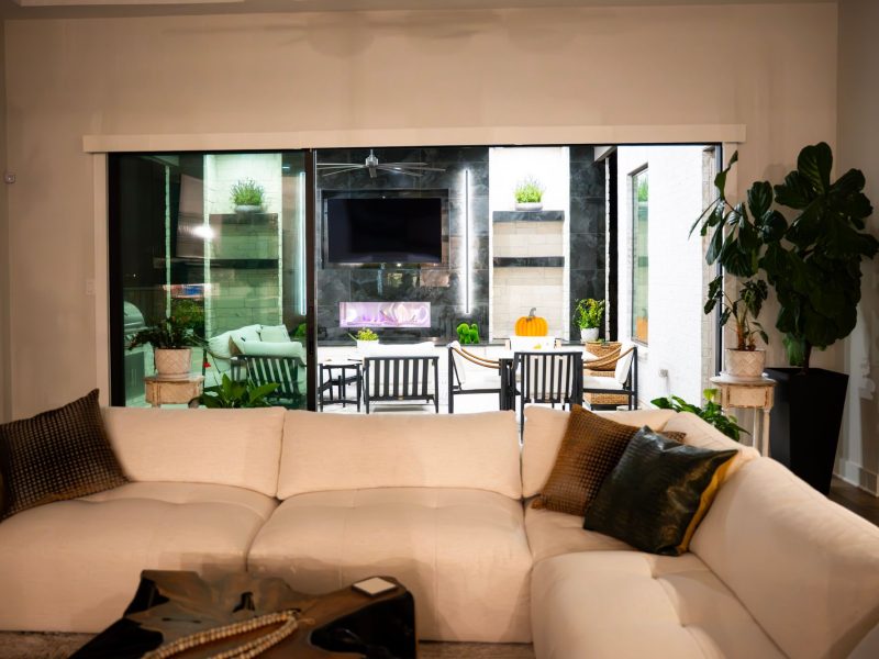 View of a modern covered patio with a fireplace, TV, and dining area seen from inside a living room.