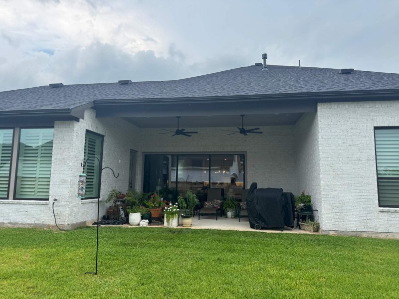 Covered patio with white brick walls, two ceiling fans, potted plants, and a covered grill.