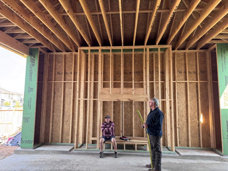 Construction progress of a patio fireplace frame with two men standing and sitting inside the wooden structure.