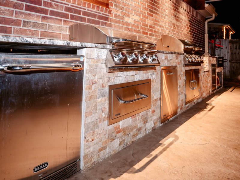 Stainless steel grills and appliances built into a stone outdoor kitchen.