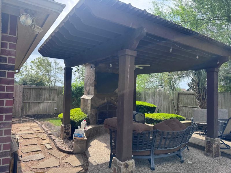 Wooden pavilion with a stone fireplace, outdoor seating area, and a stone walkway.
