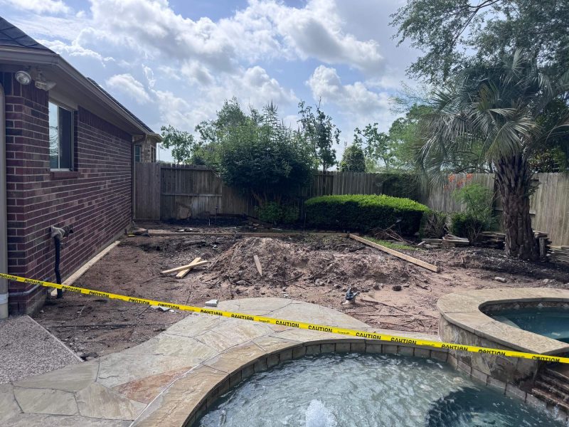 Dirt construction site for an outdoor kitchen and pavilion with yellow caution tape and a pool in the foreground.
